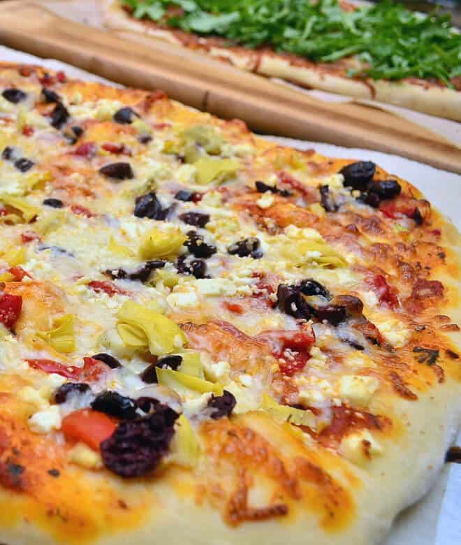 A close up image of a pizza with black olives, red peppers, and cheese.