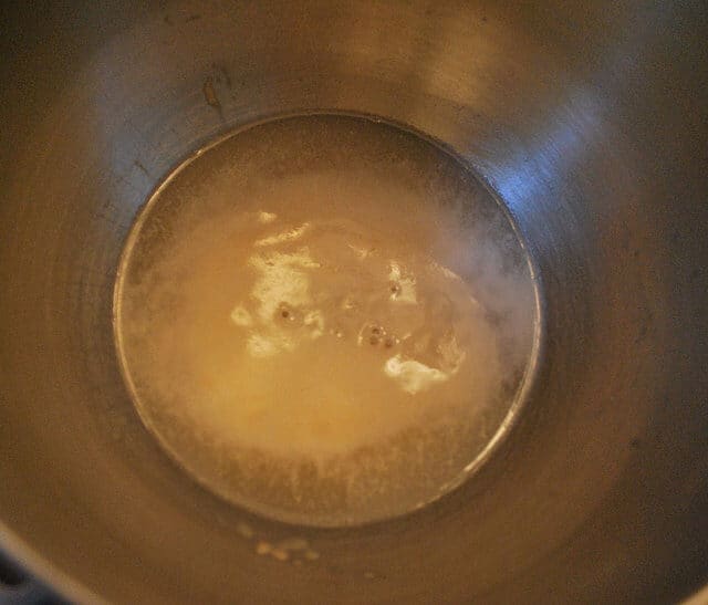 An in process image showing bubbles coming up from yeast proofing in a metal bowl.