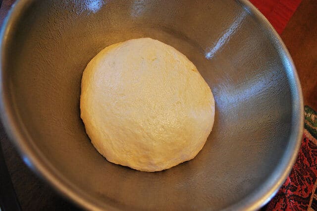 An in process image showing the ball of dough resting in the metal bowl.