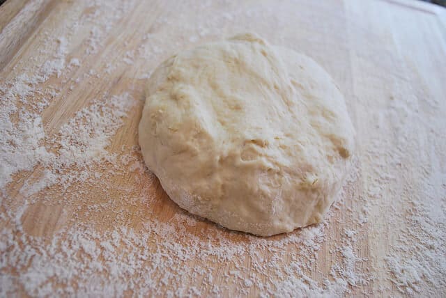 An in process image showing the ball of dough on a cutting board that has been dusted with flour.