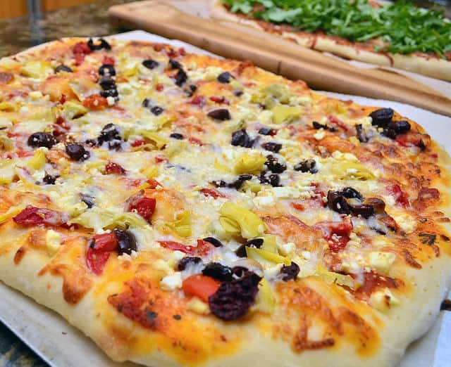 A close up image of a pizza with red peppers, olives, and cheese.