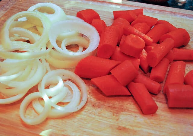 In process image showing the carrots and onions sliced on a cutting board.