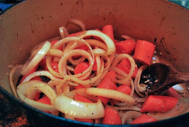 An in process image showing the carrots and onions cooking in a Dutch oven.