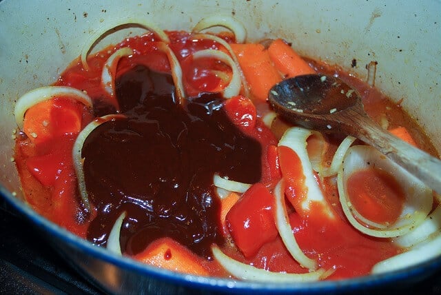An in process image showing beef broth, BBQ sauce and tomato sauce added to the Dutch oven.