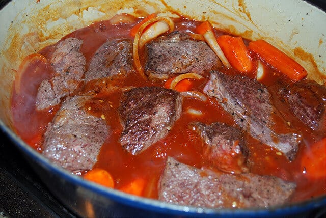 An in process image showing the ribs added to the sauce in the Dutch oven.