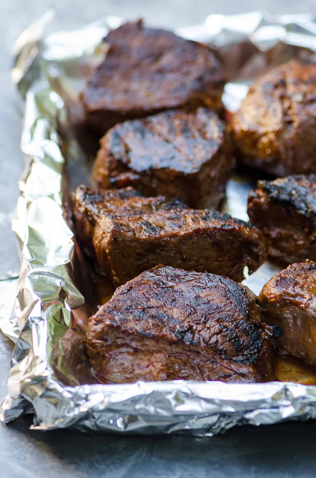 Grilled steaks on a foil lined baking sheet.