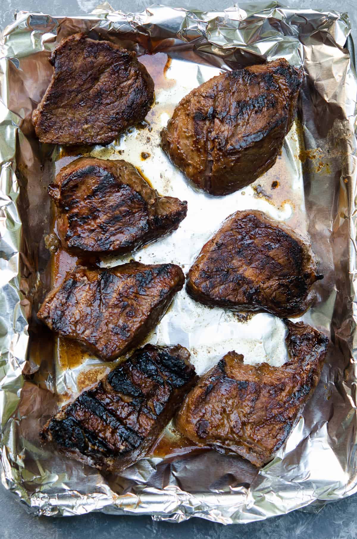 A top down shot of grilled sirloin steak on a foil lined baking sheet.