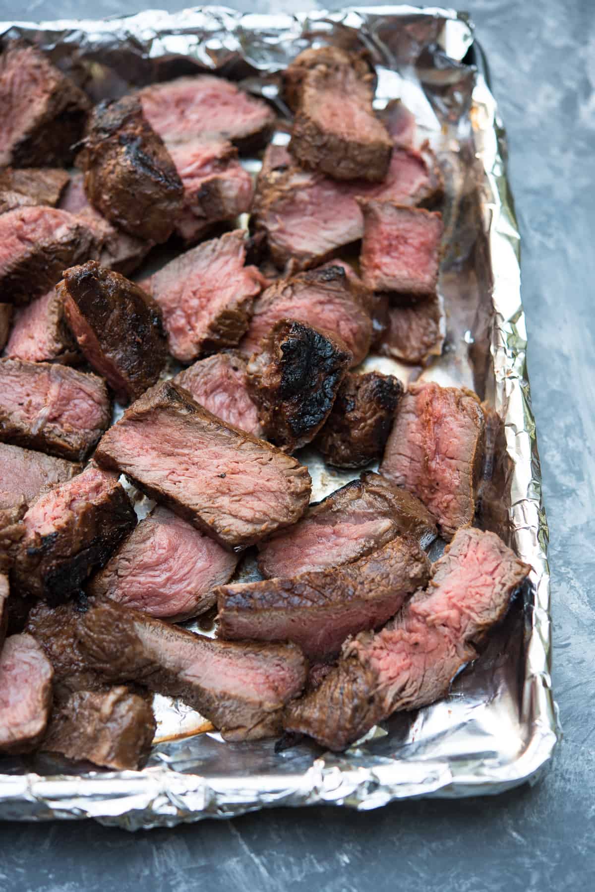 Sliced steak on a foil-lined baking sheet.
