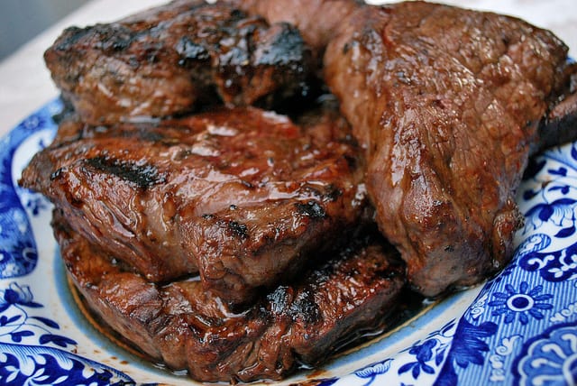 A pile of grilled steaks on a blue plate.
