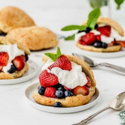 Three plates with shortcakes stuffed with fresh berries and whipped cream.