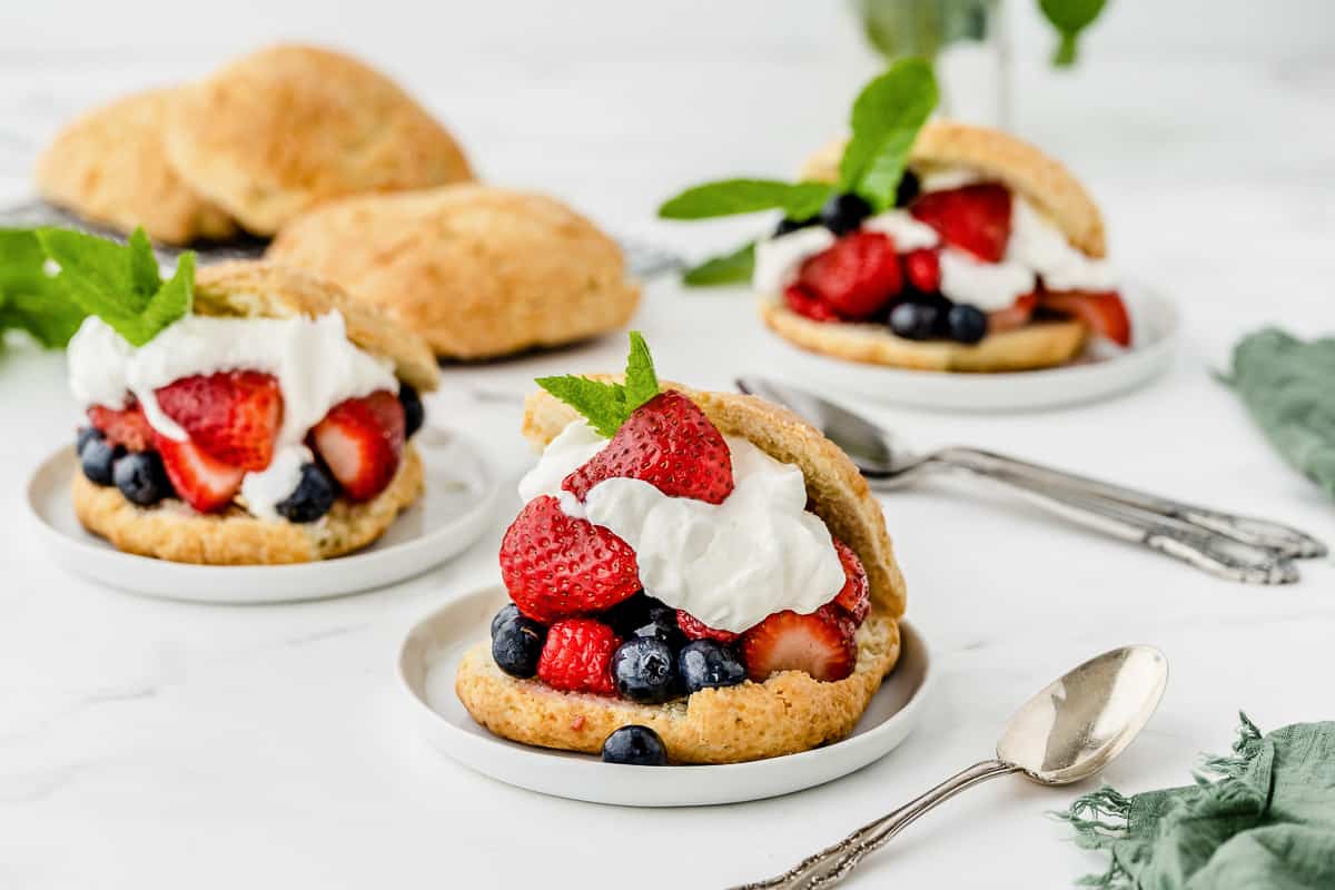 Three plates with shortcakes stuffed with fresh berries and whipped cream.