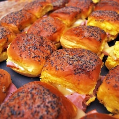 A cooking sheet covered with ham and cheese sliders.