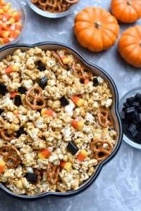 A bowl of caramel corn with mini pumpkins and candy on the side.