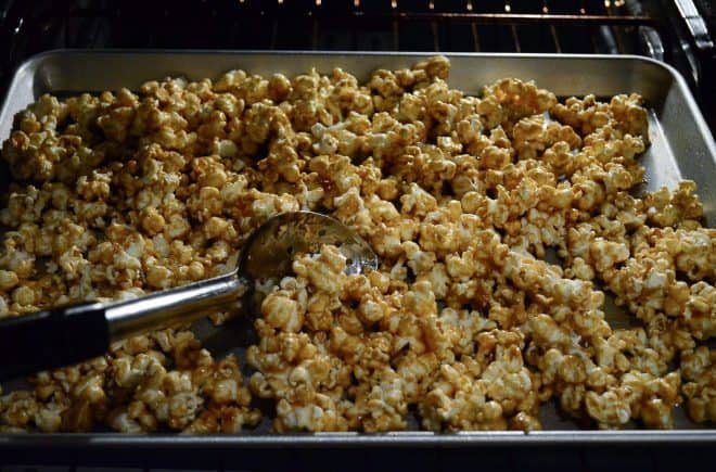 Stirring the popcorn with a spoon on a baking sheet in the oven.