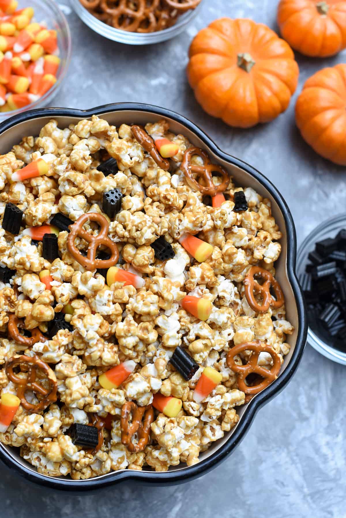 A bowl of caramel corn with mini pumpkins and candy on the side.