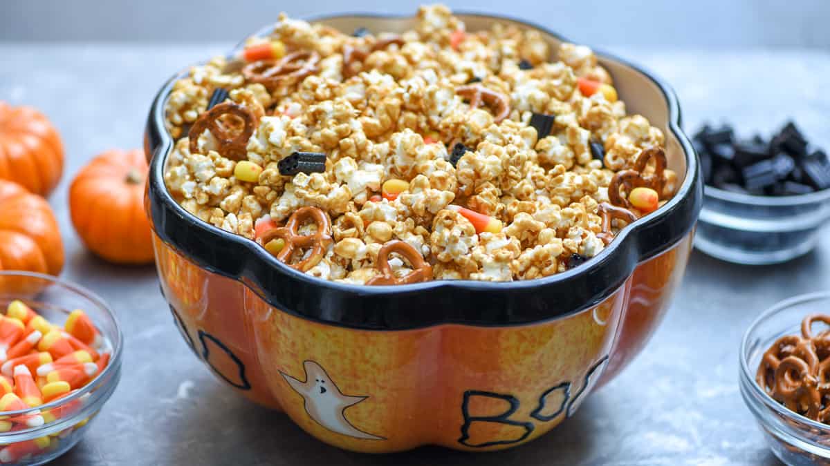 A large Halloween decorated bowl filled with caramel corn with small bowls of add ins around it.
