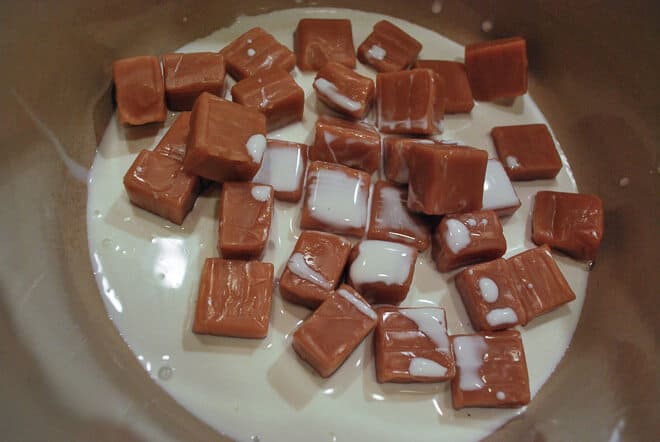 Making Caramel Oat Bars. Heavy cream and caramels are added to a saucepan.