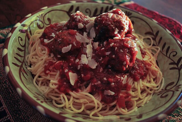 A close up image of Spaghetti and Meatballs topped with Parmesan cheese in a patterned bowl.