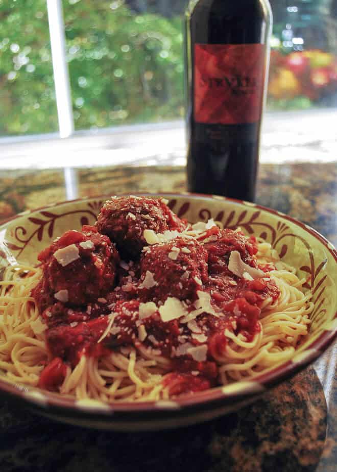 A plate of spaghetti and meatballs with a bottle of wine.