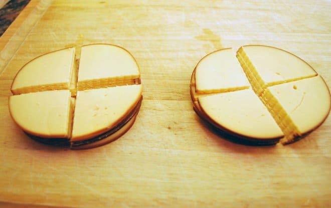 Round slices of gouda cheese stacked and sliced in quarters on a wooden cutting board.