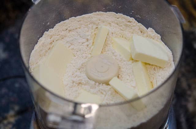 Butter is added to the flour and salt in a food processor bowl.