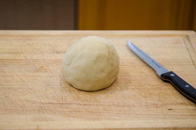 The pie pastry is formed into a ball and transferred to a wood cutting board.