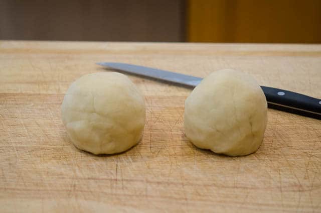 The dough is sliced in half and formed into two separate balls on a wooden cutting board.