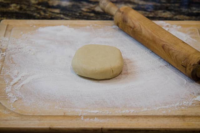 One of the balls of refrigerated dough is placed on a floured cutting board with a rolling pin next to it.