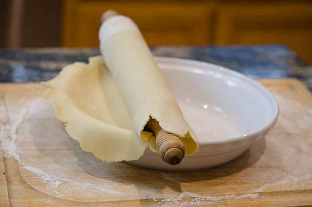 The rolling pin laying over the top of the pie dish to transfer the pastry dough.
