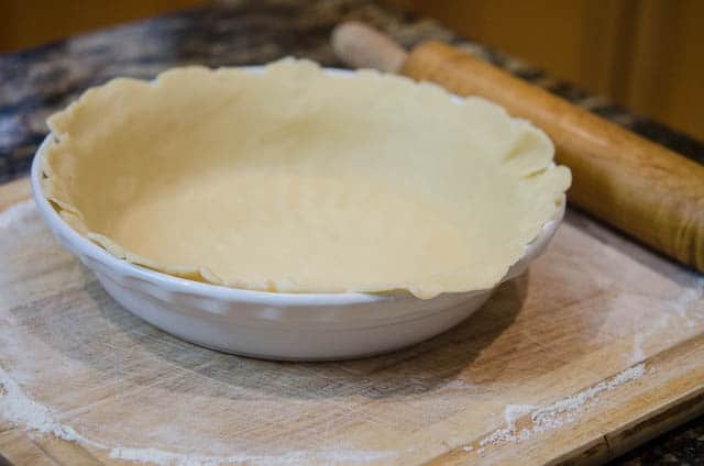 The edges of pastry dough are trimmed to fit the pie dish.
