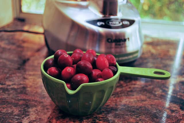 A green 1 cup measure full of fresh cranberries on a kitchen counter.