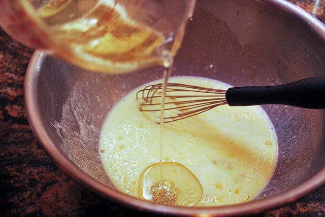 Oil is whisked into the egg and buttermilk mixture in a metal mixing bowl.