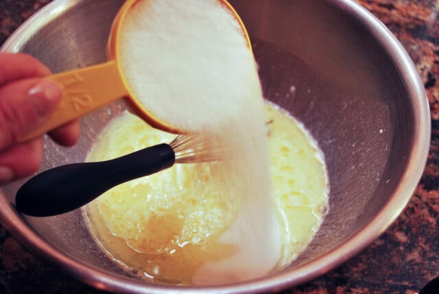 Sugar is poured into the egg mixture in the mixing bowl.