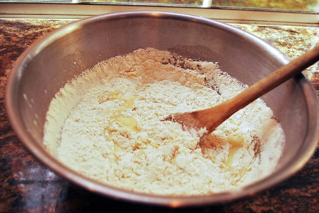 The wet ingredients are added to the mixing bowl with the dry ingredients and stirred with a wooden spoon.
