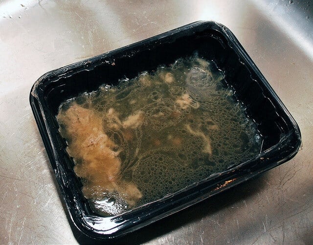 The grease is drained from the skillet into the empty meat container.