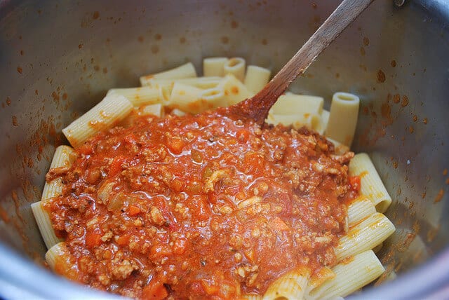 The bolognese is added to cooked rigatoni pasta in a pasta pot.