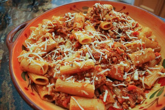 Pasta Bolognese in a large serving bowl topped with shredded Parmesan cheese.