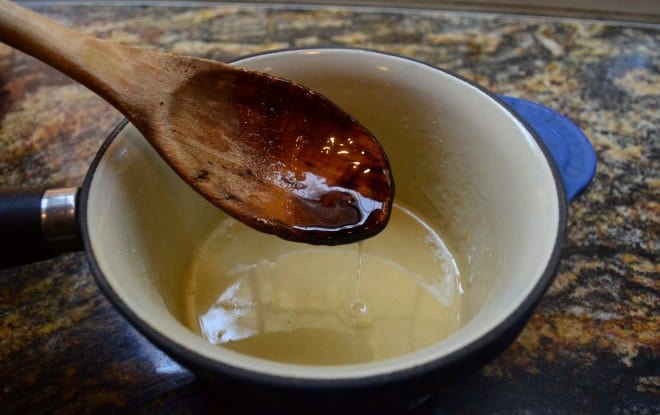 Sugar and water are cooked in a saucepan to make the simple syrup. A wooden spoon lifts some from the pan.