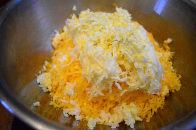 The grated cheese, butter, and egg is transferred to a large metal mixing bowl.