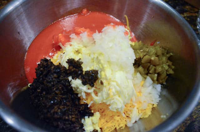 The onion, tomato soup, olives, green chiles, salt and pepper are added to the cheese mixture in the metal mixing bowl.
