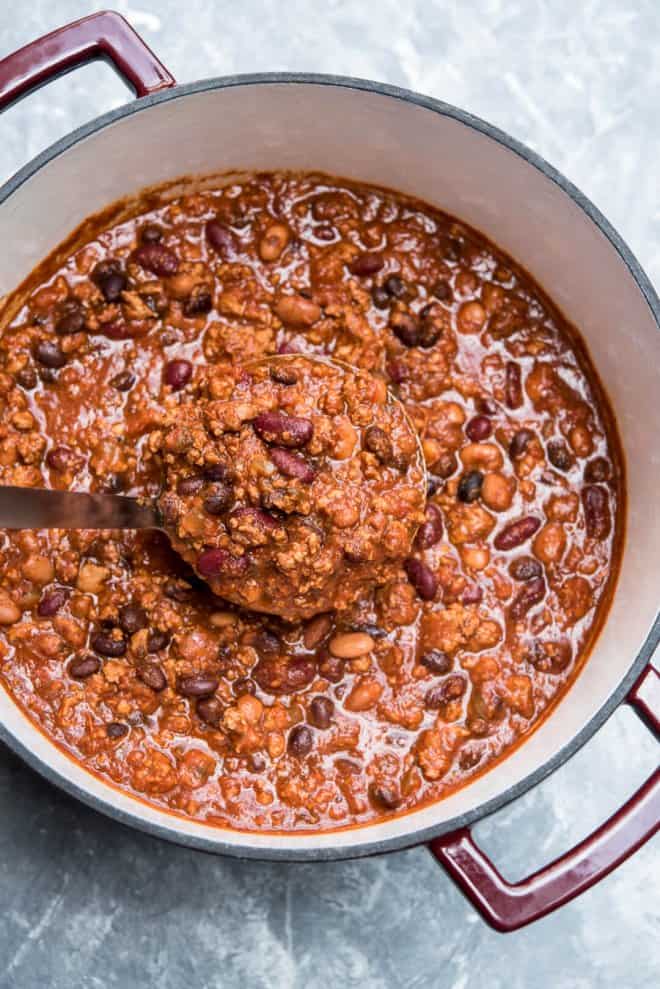A ladle full of Three Bean Turkey Chili is lifted from of a Dutch oven. Easy pantry staple recipes.