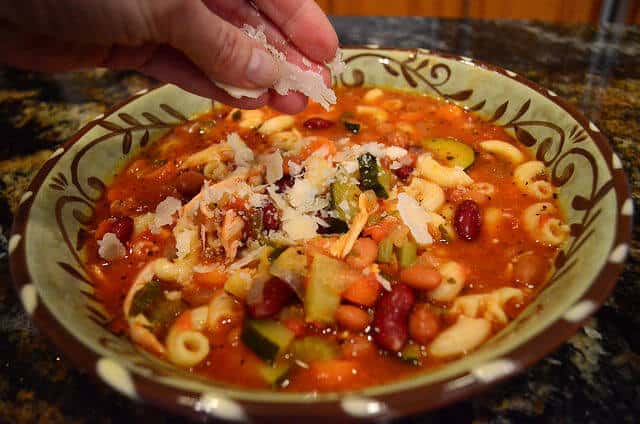 A bowl of Bonnie's minestrone with Parmesan cheese being sprinkled on top.