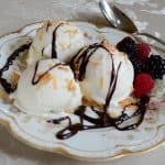 A serving of ice cream with berries and chocolate syrup.