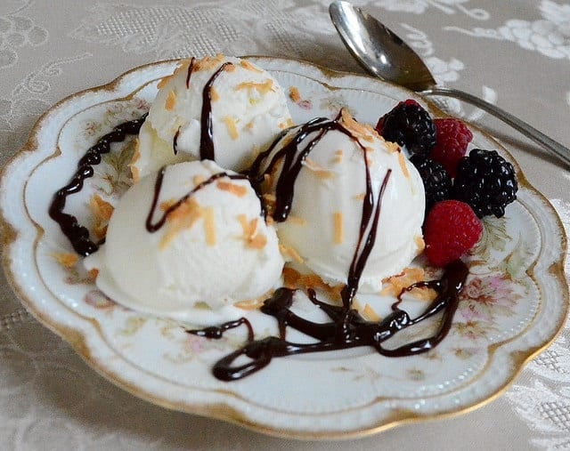 Coconut Ice Cream on a decorative plate with chocolate sauce drizzled on top and a side of raspberries and black berries.