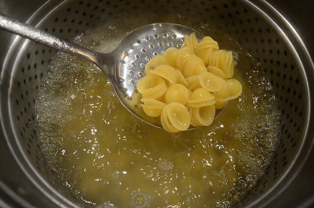 A spoonful of orecchiette pasta being spooned out from a boiling pot.