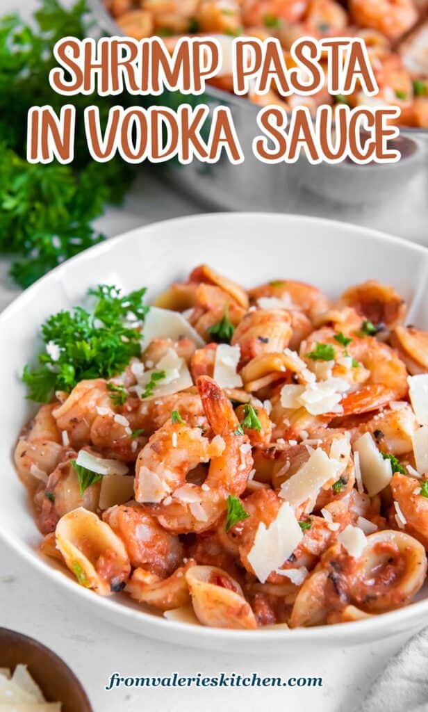 A white bowl filled with orecchiette pasta with shrimp in a vodka sauce garnished with shaved Parmesan and parsley with text.