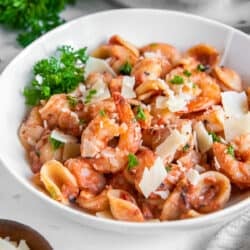 A white bowl filled with orecchiette pasta with shrimp in a vodka sauce garnished with shaved Parmesan and parsley.