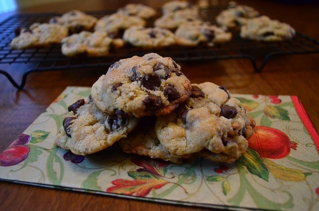 Toffee Chocolate Chip Cookies on a napkin with a cooling rack filled with cookies behind them.