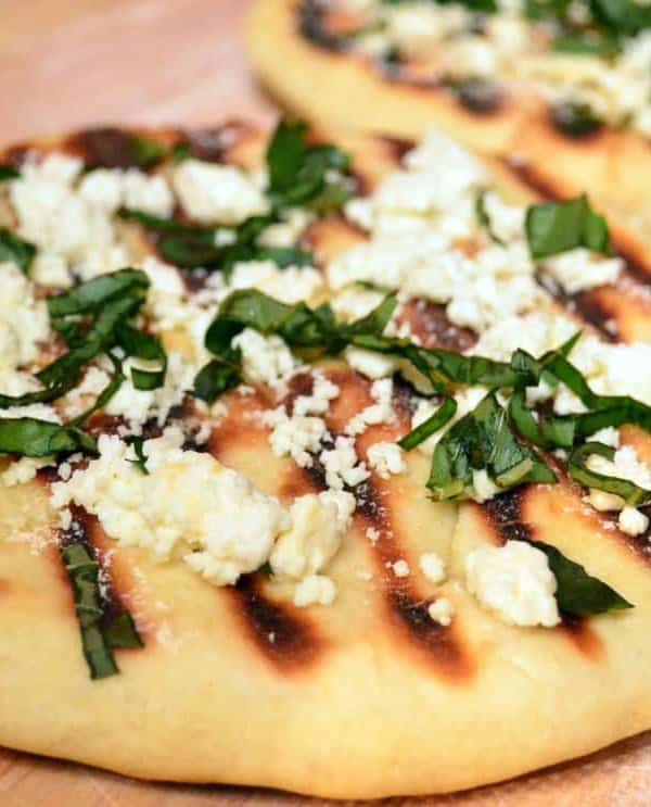A close up of flatbread with feta and basil on top.