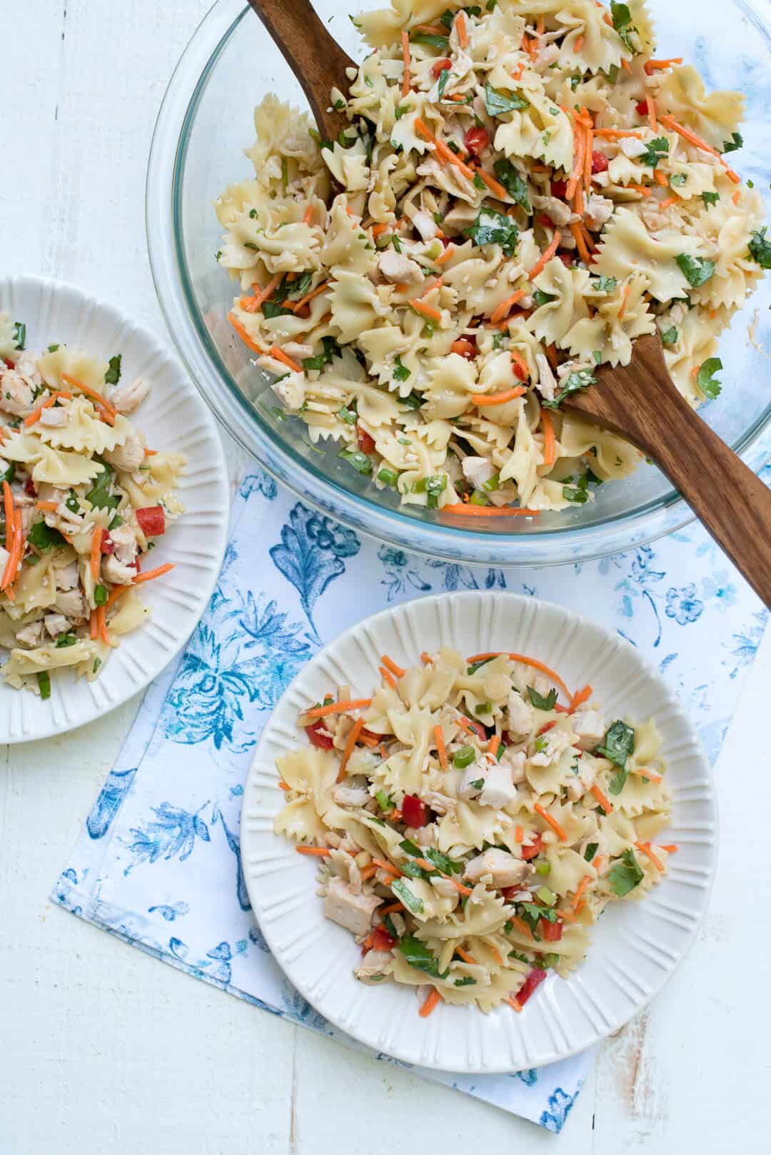 A serving bowl and two plates with Asian Pasta Salad.